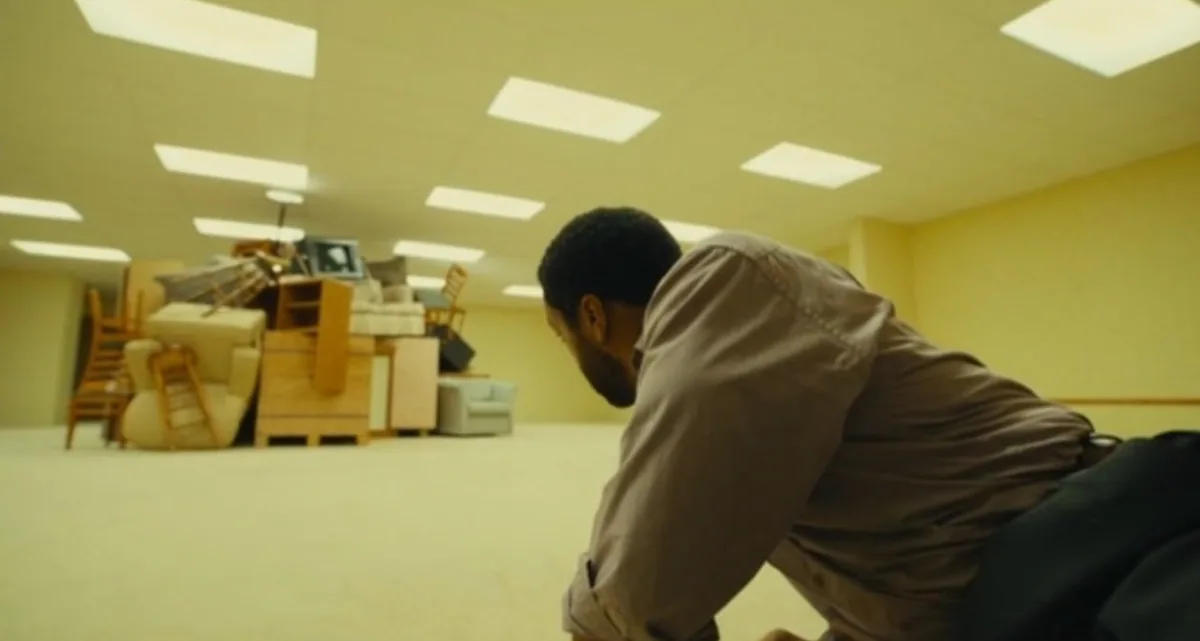 A man on the floor of a yellow room beneath fluorescent lights in Backrooms.