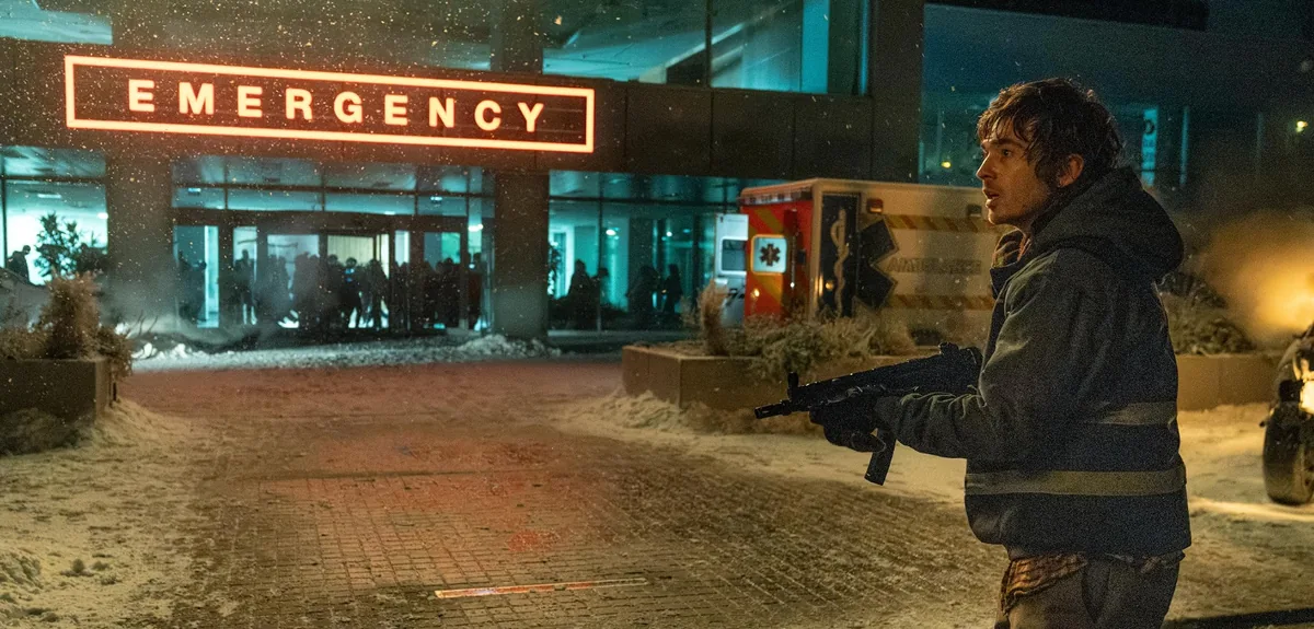 A man holding a firearm outside a snow-covered emergency entrance at night in Resident Evil (2026).